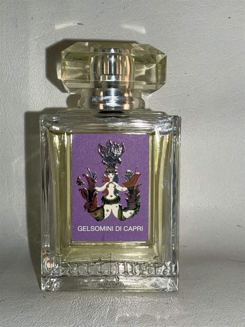 May include: A clear glass bottle of perfume with a silver cap. The bottle has a purple label with a gold illustration of a mermaid and the text 'Gelsomini di Capri'.