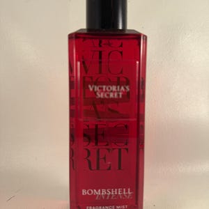 May include: A red rectangular fragrance mist bottle with a black cap. The bottle has the words "VICTORIA'S SECRET" and "BOMBSHELL INTENSE" printed on it. It contains 8.4 fl oz (250ml) of fragrance mist.