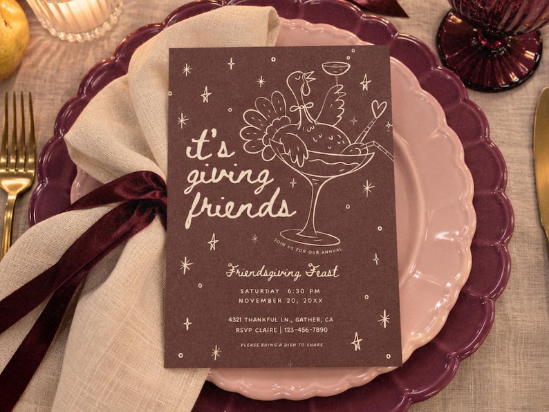 Photorealistic flat lay of a whimsical Friendsgiving invitation printed on a dark mauve brown card with blush pink hand-drawn cocktail glass, bows, stars, and “it's giving friends” lettering. Styled on a scalloped pink dinner plate with soft fabric and ribbon details. This editable Canva Thanksgiving dinner invitation features a playful retro design with customizable text and colors, available as a printable or digital fall party invite.