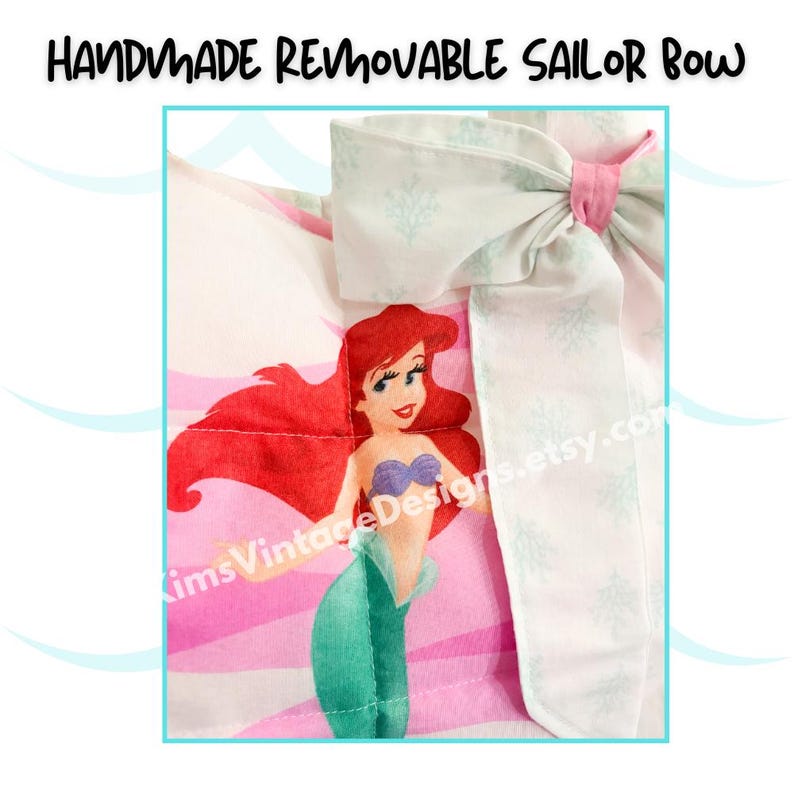 May include: Handmade removable sailor bow featuring a cartoon mermaid with red hair, a purple top, and a green tail. The bow is white with a light blue pattern and a pink center. The text "Handmade Removable Sailor Bow" is at the top.