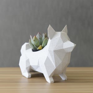 May include: White geometric ceramic planter shaped like a dog, with a small succulent plant inside.