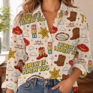 May include: A long-sleeve button-down shirt with a white base featuring a repeating pattern of brown cowboy boots, red cowboy hats, yellow sheriff stars, alphabet blocks, and the text "I KNEW IT I KNEW YOU" and "infinity and beyond".