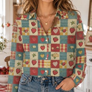 May include: A button-down shirt with a patchwork design featuring strawberries, hearts, and floral elements in red, yellow, and blue squares. The shirt is worn with blue jeans. The background includes a kitchen setting with a sign that says "Strawberries".