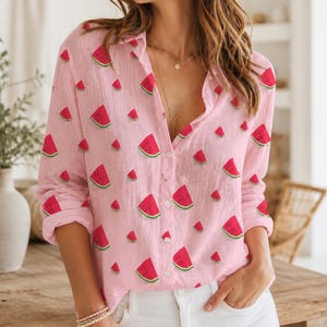 Op de afbeelding: Roze overhemd met knopen en een patroon van rode watermeloenpartjes. Het shirt met lange mouwen heeft een kraag en is gemaakt van een lichte stof. De watermeloenpartjes hebben groene schillen.