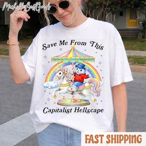 May include: White t-shirt featuring a carousel design with a bear riding a unicorn, a rainbow, and the text "Save Me From This Capitalist Hellscape". The shirt has a crew neck and short sleeves.