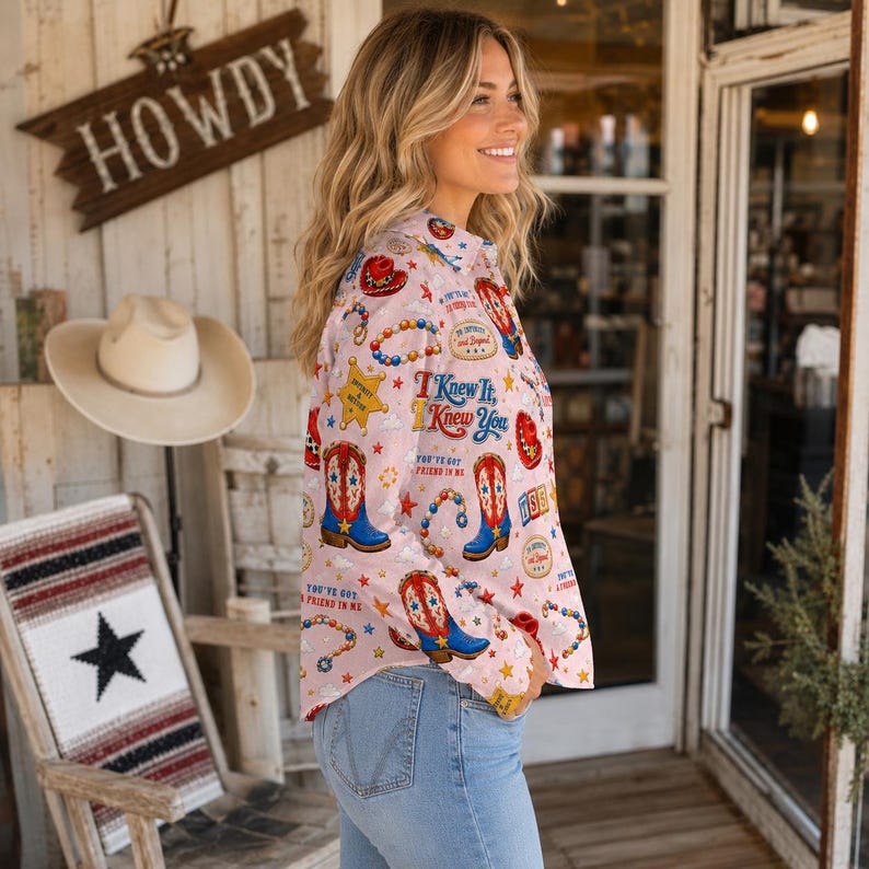 May include: A light pink long-sleeve button-down shirt featuring a repeating pattern of cowboy boots, sheriff stars, beaded necklaces, and cowboy hats. The shirt includes text that reads I Knew It, I Knew You and You've Got A Friend In Me.