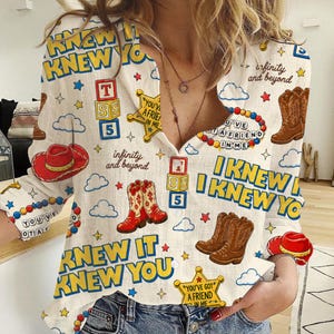 May include: A long-sleeved button-down shirt in off-white featuring a repeating print of brown cowboy boots, red cowboy hats, yellow sheriff stars, alphabet blocks, and colorful beads. The text reads "I KNEW IT I KNEW YOU" and "YOU'VE GOT A FRIEND IN ME".