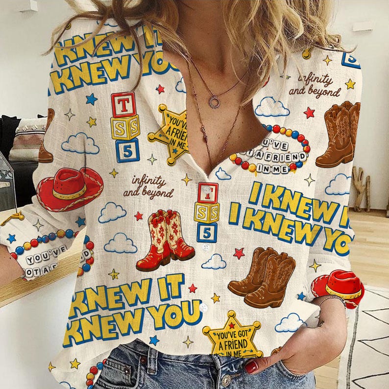 May include: A long-sleeved button-down shirt in off-white featuring a repeating print of brown cowboy boots, red cowboy hats, yellow sheriff stars, alphabet blocks, and colorful beads. The text reads "I KNEW IT I KNEW YOU" and "YOU'VE GOT A FRIEND IN ME".