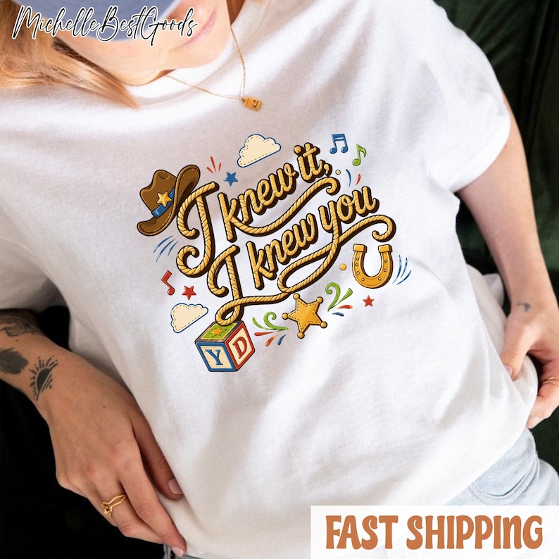 K&ouml;nnte beinhalten: Ein wei&szlig;es T-Shirt mit einem grafischen Design und dem Text "I knew it, I knew you" in einer seilartigen Schriftart. Das Design enth&auml;lt einen braunen Cowboyhut, ein gelbes Hufeisen, einen bunten Buchstabenw&uuml;rfel mit den Buchstaben Y und D sowie Sterne.