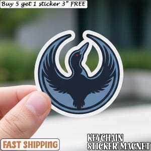 May include: A round sticker featuring a stylized bird emblem in shades of blue and black, with a red eye. The sticker is held by a hand. Text on the sticker reads "KEYCHAIN STICKER/MAGNET". The sticker is approximately 3 inches in diameter.