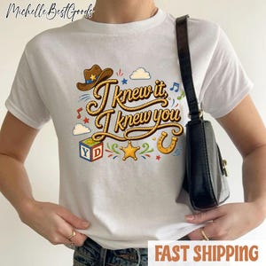 K&ouml;nnte beinhalten: Ein wei&szlig;es T-Shirt mit kurzen &Auml;rmeln und einem Grafikdruck mit dem Text I knew it, I knew you in brauner Seil-Optik. Das Design enth&auml;lt einen braunen Cowboyhut, einen bunten Buchstabenw&uuml;rfel, einen gelben Stern und ein Hufeisen-Symbol.