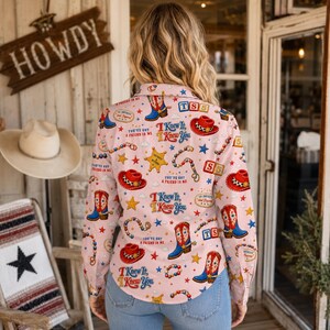 May include: A long-sleeve button-down shirt in light pink featuring a repeating pattern of blue cowboy boots, red cowboy hats, yellow sheriff stars, and beaded necklaces. The text "I Knew It, I Knew You" and "You've Got a Friend in Me" is printed.