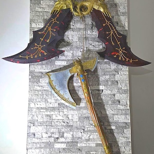 May include: A display featuring two large, ornate blades suspended above a detailed axe. The blades are dark with red and gold accents, while the axe has a silver blade and a wooden handle with gold detailing. The items are mounted on a gray brick wall.