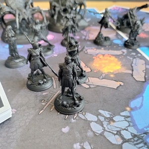 May include: A collection of black painted miniature figurines on a game board with a blue and gray design. The figurines are of various characters, including a knight, a warrior, and a creature.