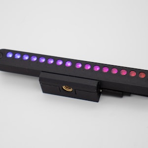 May include: A black electronic device with a series of multi-colored lights. The lights transition from blue to purple to pink to red. The device has a mounting bracket and a black cable.
