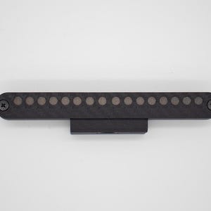 May include: A black, rectangular electronic component featuring a horizontal row of fifteen circular metallic contacts. The device is secured with a Phillips head screw on each end and includes a central mounting bracket on the bottom edge.