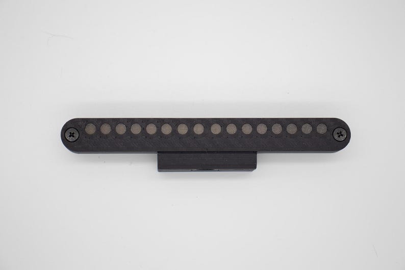 May include: A black, rectangular electronic component featuring a horizontal row of fifteen circular metallic contacts. The device is secured with a Phillips head screw on each end and includes a central mounting bracket on the bottom edge.