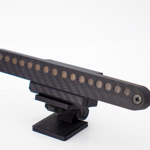 May include: A black carbon fiber textured horizontal bar featuring a row of twelve circular metallic contacts. The bar is mounted on a black plastic adjustable base with a pivot joint and is secured at both ends with visible metal screws.
