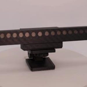 May include: A black, horizontal, rectangular camera accessory featuring a row of fourteen circular, metallic-colored sensors or lights embedded along its front face. The device includes a mounting base with a screw mechanism for attachment.