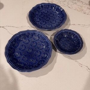 May include: Three deep blue ceramic bowls of varying sizes, each featuring a repeating embossed hexagonal pattern with floral motifs and scalloped edges. The bowls have a glossy finish and a consistent dark blue color throughout the set.
