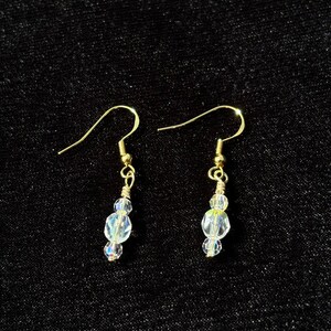 Dainty and elegant clear iridescent glass bead earrings dangle from a gold hook