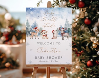 May include: A wooden easel displays a baby shower sign with a winter theme. The sign features watercolor illustrations of animals wearing Santa hats and scarves. Text includes "Baby it's cold outside" and "Welcome to Samantha's Baby Shower."