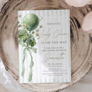 May include: A baby shower invitation card with a green balloon, shamrocks, and the text "Our Little Lucky Charm Is On The Way." The invitation is on a striped background and includes event details. The card is placed on a decorative wooden plate.