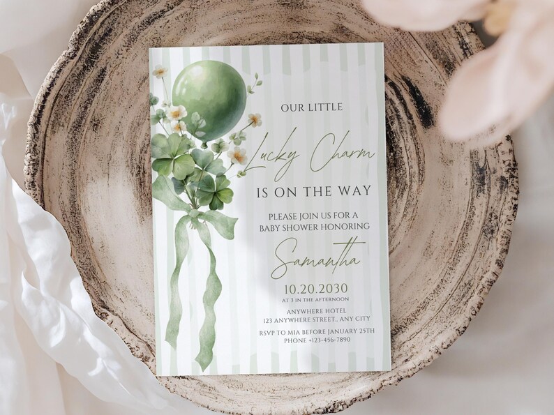 May include: A baby shower invitation card with a green balloon, shamrocks, and the text "Our Little Lucky Charm Is On The Way." The invitation is on a striped background and includes event details. The card is placed on a decorative wooden plate.