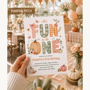 May include: A white rectangular birthday invitation card featuring the text It's FUN to be ONE and Charlotte's First Birthday. The design includes watercolour illustrations of orange and white pumpkins, pink bows, butterflies, and floral accents.