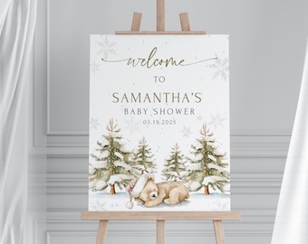 Może przedstawiać: Znak powitalny na baby shower na sztaludze. Znak zawiera napis "welcome to SAMANTHA'S BABY SHOWER 03.19.2025" ze sceną zimowego lasu i śpiącym misiem w czapce Świętego Mikołaja. Przedstawione są również płatki śniegu i sosny.
