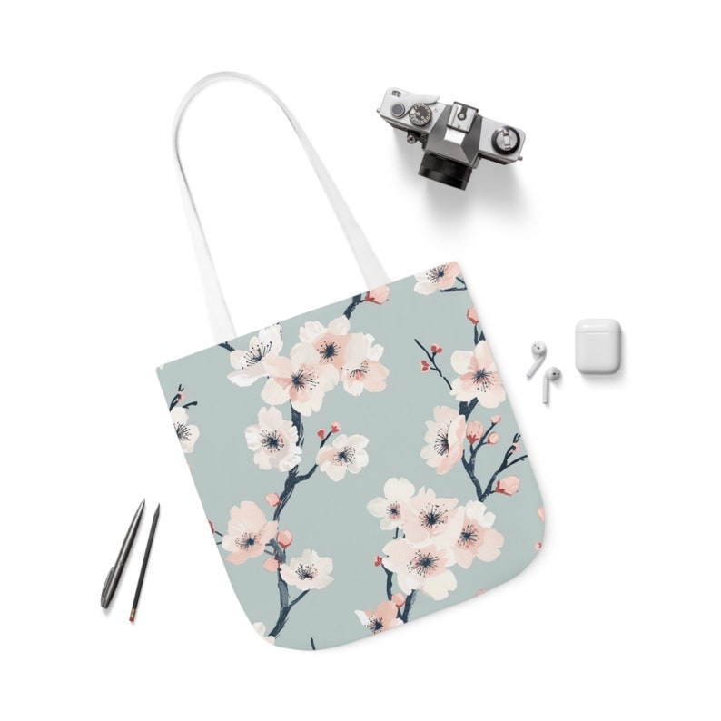 Elegant canvas tote bag with a serene cherry blossom print in pastel shades on a soft blue background, combining style and practicality for everyday use.