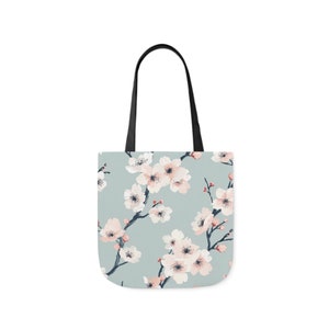 Elegant canvas tote bag with a serene cherry blossom print in pastel shades on a soft blue background, combining style and practicality for everyday use.