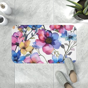 A foam bath mat featuring a lush watercolor painting of vibrant flowers in shades of pink, blue, and yellow, offering a stylish and comfortable addition to bathroom decor.
