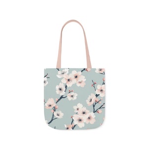 Elegant canvas tote bag with a serene cherry blossom print in pastel shades on a soft blue background, combining style and practicality for everyday use.