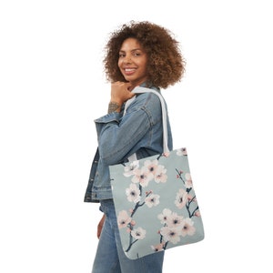 Elegant canvas tote bag with a serene cherry blossom print in pastel shades on a soft blue background, combining style and practicality for everyday use.