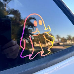 May include: A holographic sticker of a ghost giving the middle finger. The ghost is outlined in a rainbow color gradient.