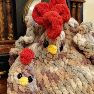 May include: A handmade, plush chicken-shaped bag with a matching keychain. The bag features a red comb, black eyes, and a yellow beak. The body is made of soft, multicolored yarn in shades of brown, gray, and purple.