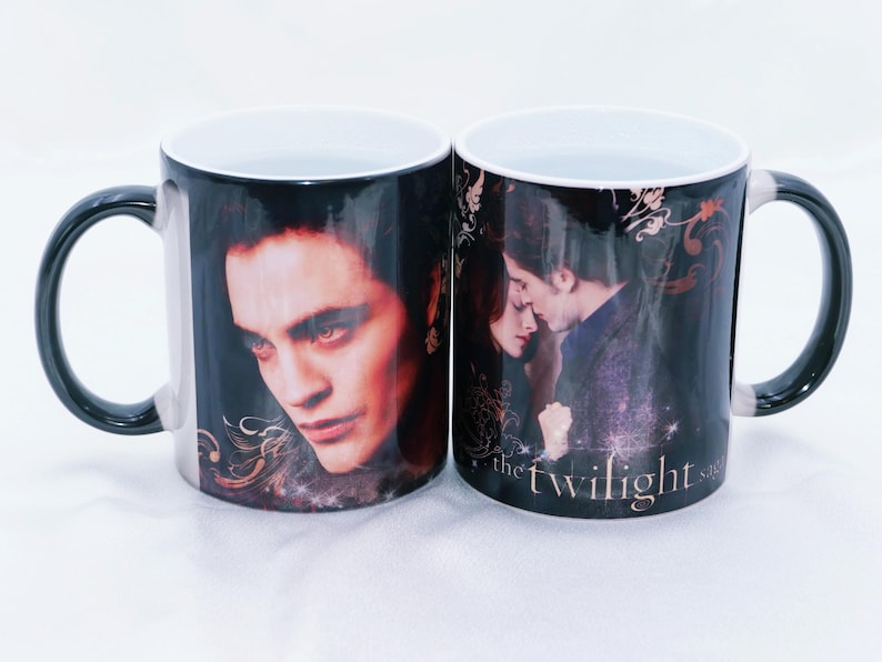 May include: Two ceramic mugs with black handles and rims. Each mug features a different image of characters from the Twilight saga. The text "the twilight saga" is visible on one mug.