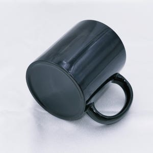 May include: A black ceramic mug with a glossy finish. The mug has a cylindrical shape with a rounded handle. The mug is designed for hot or cold beverages and is suitable for home or office use.