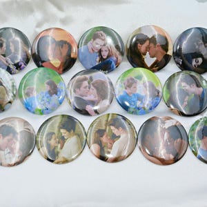 May include: A collection of fifteen round, glossy buttons featuring romantic images of a couple. The buttons display various scenes of the couple embracing and kissing, with a soft, blurred background. The buttons are arranged on a white surface.