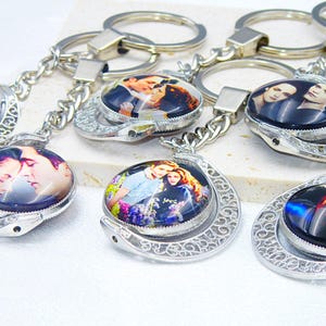 Puede incluir: Seis llaveros de plata con un diseño circular. Cada llavero presenta una imagen diferente de una pareja. Los llaveros están unidos a anillas de plata.