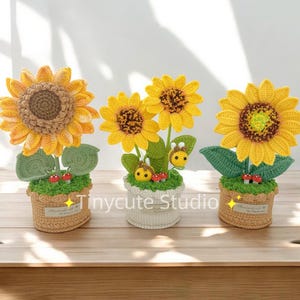 May include: Three crocheted sunflower arrangements in pots. Each sunflower is yellow with a brown center. The pots are brown, white, and beige. The sunflowers are surrounded by green leaves and red mushrooms. The text "Tinycute Studio" is visible in the image.