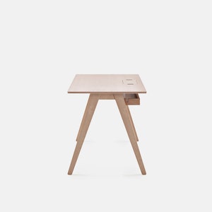 May include: A light wood desk with a drawer and a cut-out for cords on the top. The desk has a simple, modern design with angled legs.