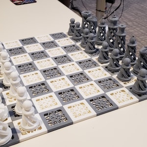 Puede incluir: Un juego de ajedrez blanco y gris con piezas de diseño intrincado. El tablero de ajedrez está hecho de un material blanco y gris con un diseño estampado.