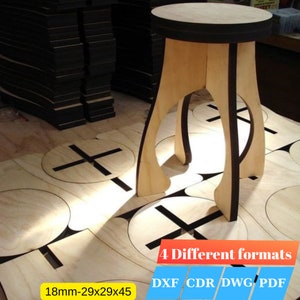 Op de afbeelding: Een houten kruk met een zwarte rand, 18 mm dik en met afmetingen van 29x29x45 cm. De kruk is gemaakt van multiplex en heeft een eenvoudig, modern ontwerp. De afbeelding toont ook meerdere uitgesneden stukken hout met een kruisvorm, wat suggereert dat het een doe-het-zelfproject is.