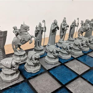 Könnte beinhalten: Ein Schachspiel in Grau und Weiß mit einem Schachbrett in Blau und Grau. Die Schachfiguren sind aus Kunststoff und im Stil mittelalterlicher Ritter und Könige. Das Schachbrett ist aus hartem Kunststoff und hat eine glänzende Oberfläche.