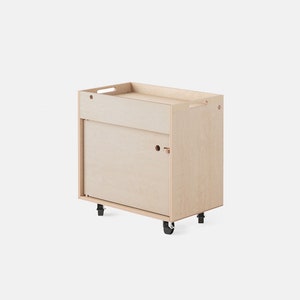 Peut inclure: Un chariot roulant en bois clair avec un tiroir coulissant et un plateau supérieur. Le chariot a deux roues de chaque côté.