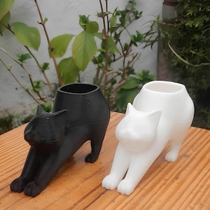 May include: Two ceramic cat planter pots, one black and one white, in a stretching pose. The pots are designed to hold small plants or succulents.