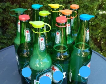 May include: A group of green glass beer bottles with colorful bottle stoppers. The stoppers have a loop handle and are in various colors, including blue, green, yellow, orange, and red.