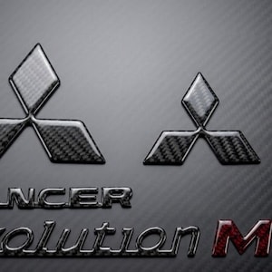 May include: Two carbon fibre Mitsubishi logos, one large and one small, above the words "Lancer Evolution MR" on a textured black background. The MR is in red carbon fibre.